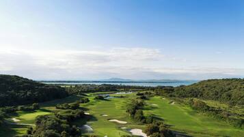 A golf course with a water body in the background, surrounded by greenery.