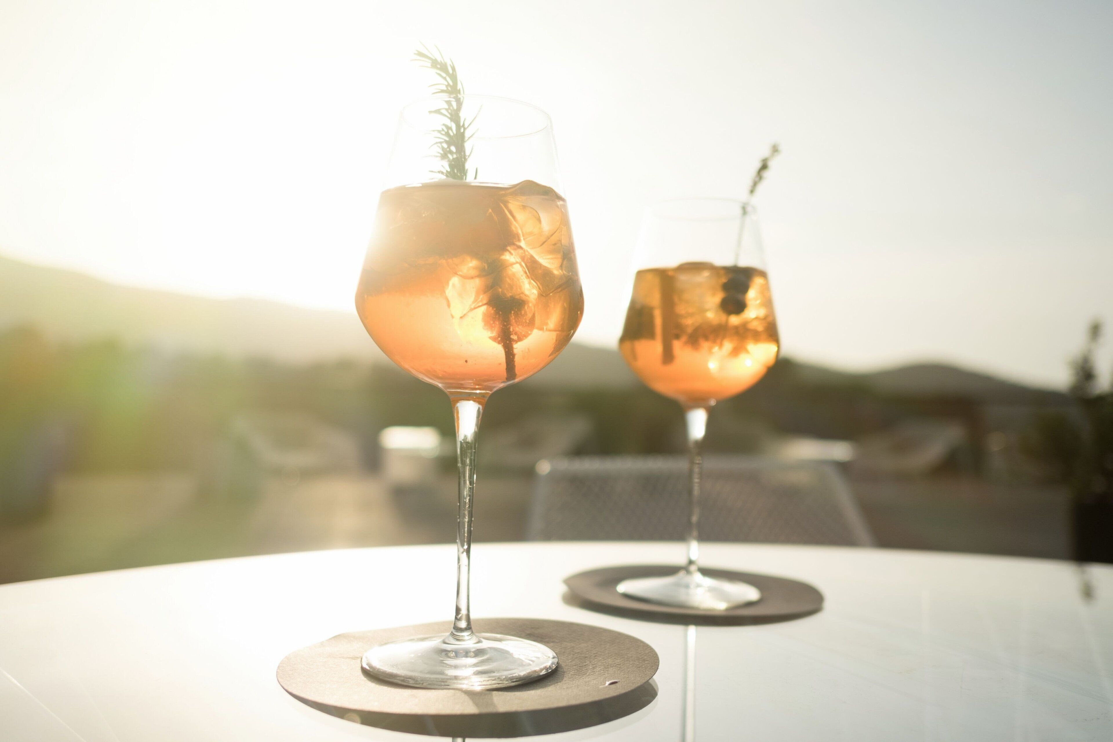 Two glasses of a beverage with a garnish on a table with a view of the outdoors.