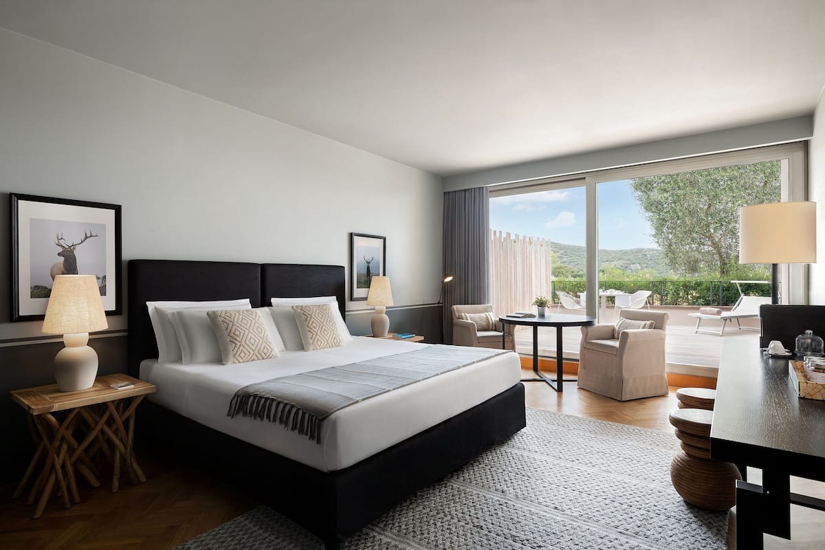 A modern hotel room with a large bed, a desk, and a view of the outdoors.