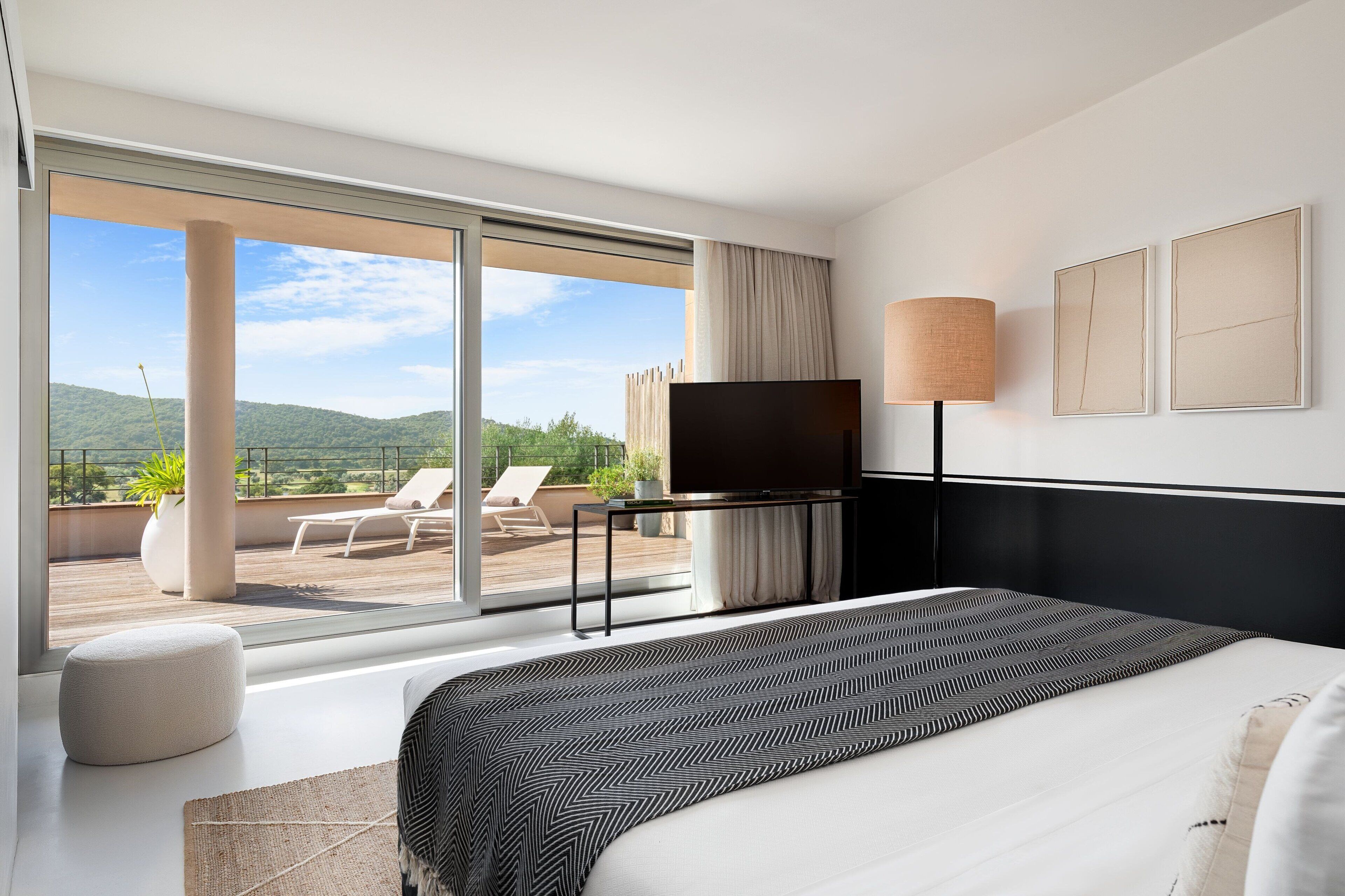 A modern hotel room with a large bed, a flat-screen TV, a bedside table, and a view of the outdoors.