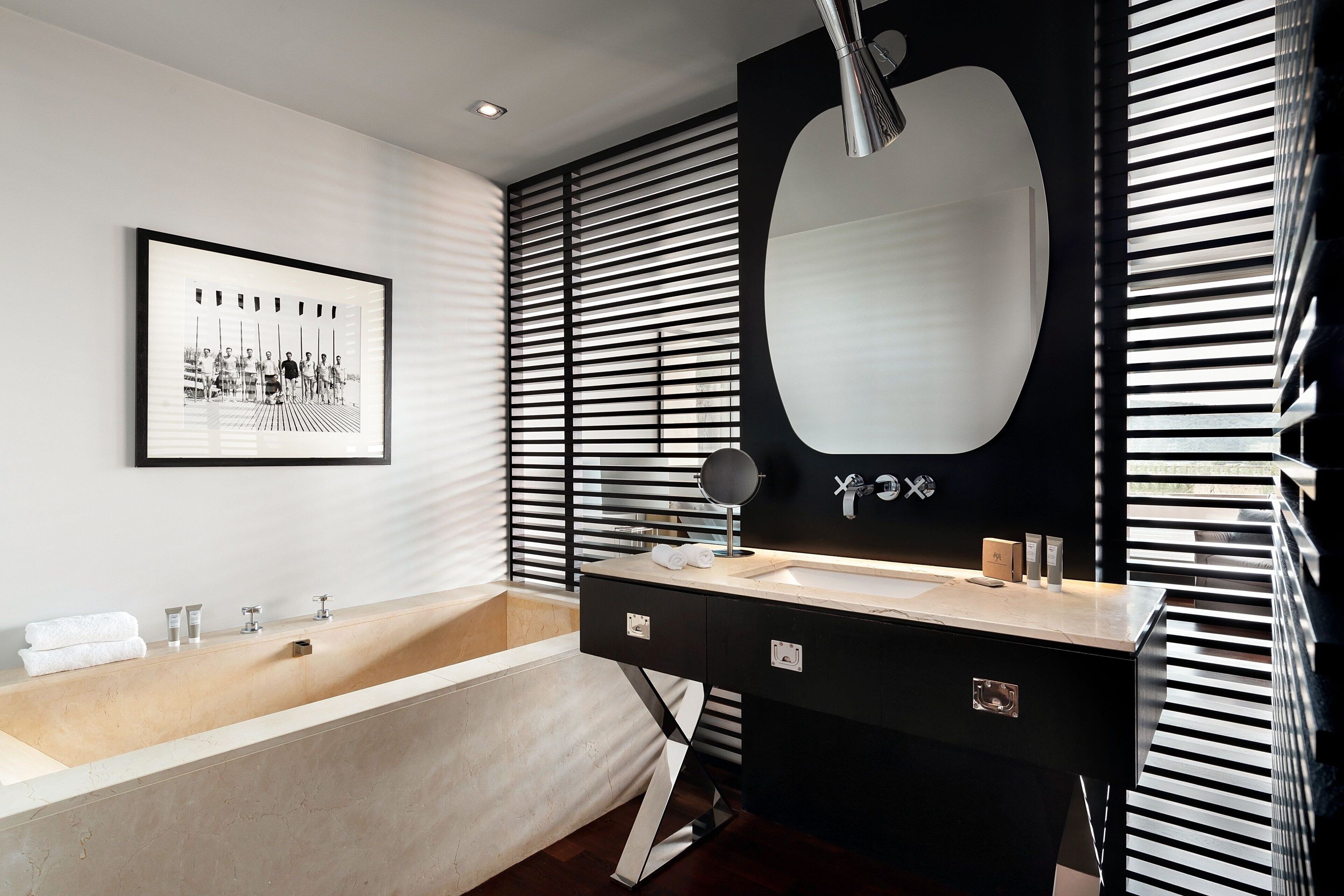 A modern bathroom with a bathtub, a large mirror, and a framed black and white photograph on the wall.