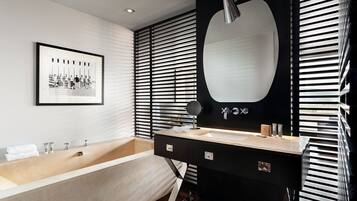 A modern bathroom with a bathtub, a large mirror, and a framed black and white photograph on the wall.