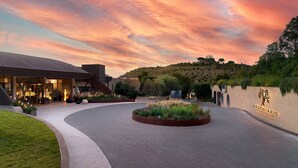 A landscaped entrance area with a curved pathway leading to a building with a modern design, featuring a landscaped garden and a sign with the name "ARGENTARIO".