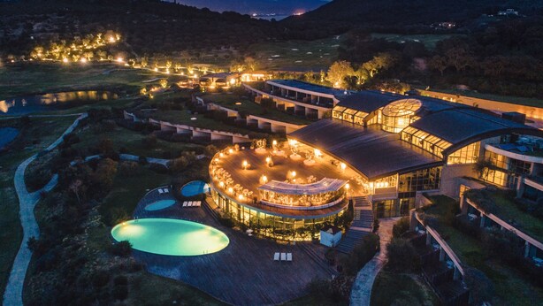A modern hotel with a circular central courtyard, multiple swimming pools, and a large glass conservatory.