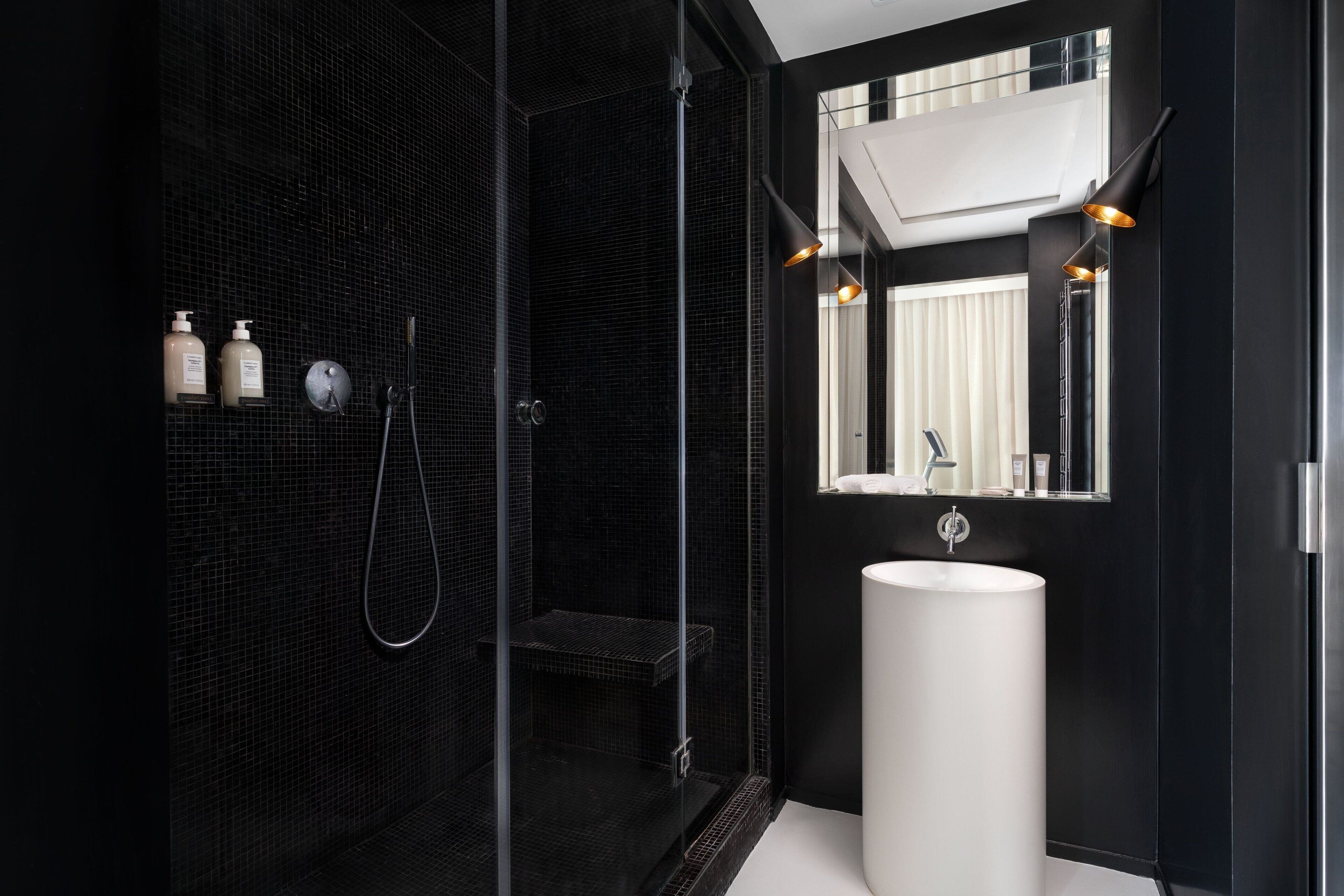 A modern bathroom with a black tiled shower, a white sink, and a mirror above it.