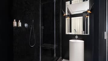 A modern bathroom with a black tiled shower, a white sink, and a mirror above it.