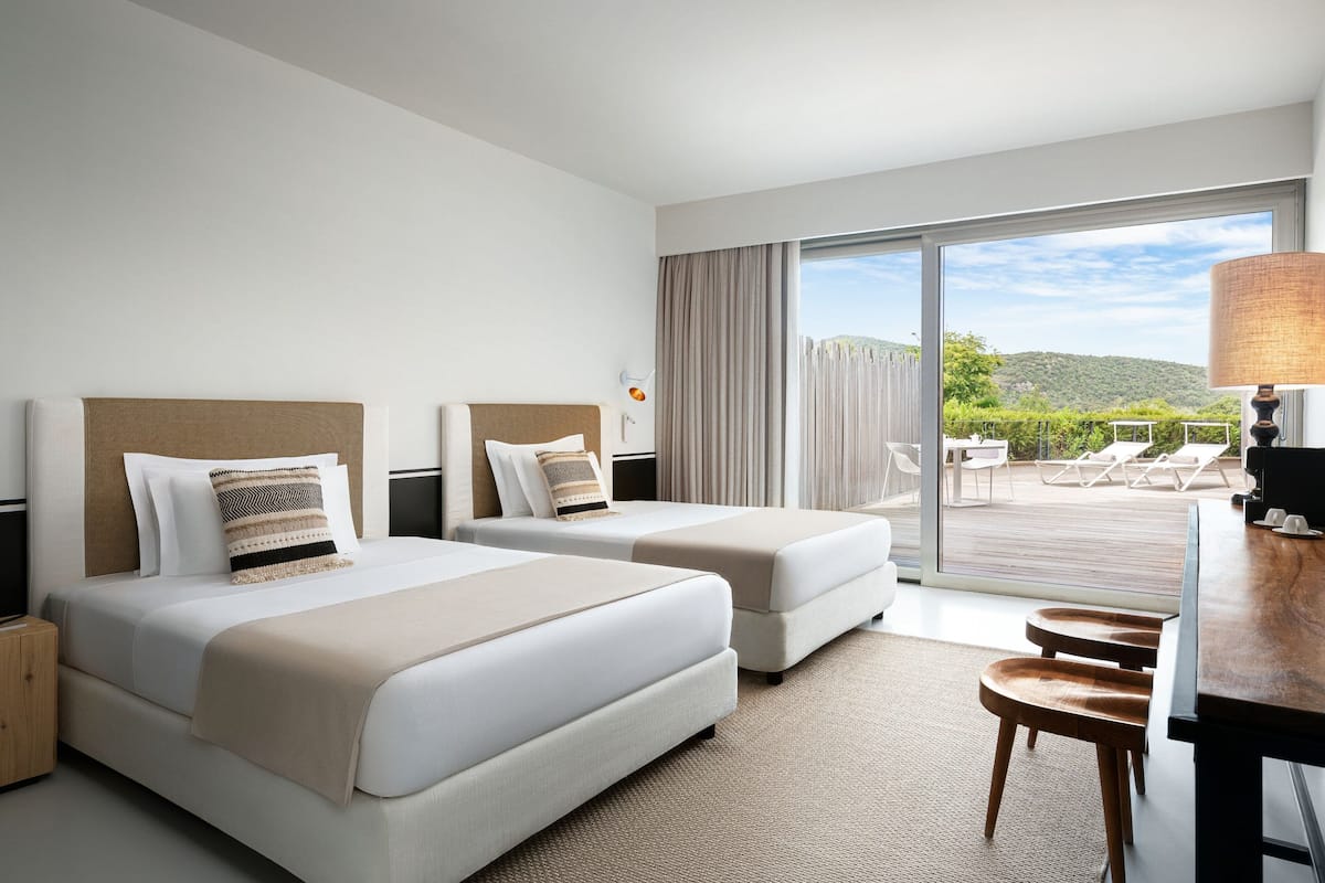 A hotel room with two beds, a desk, and a view of the outdoors.
