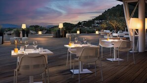 An outdoor dining area with tables and chairs, set against a backdrop of a sunset sky.