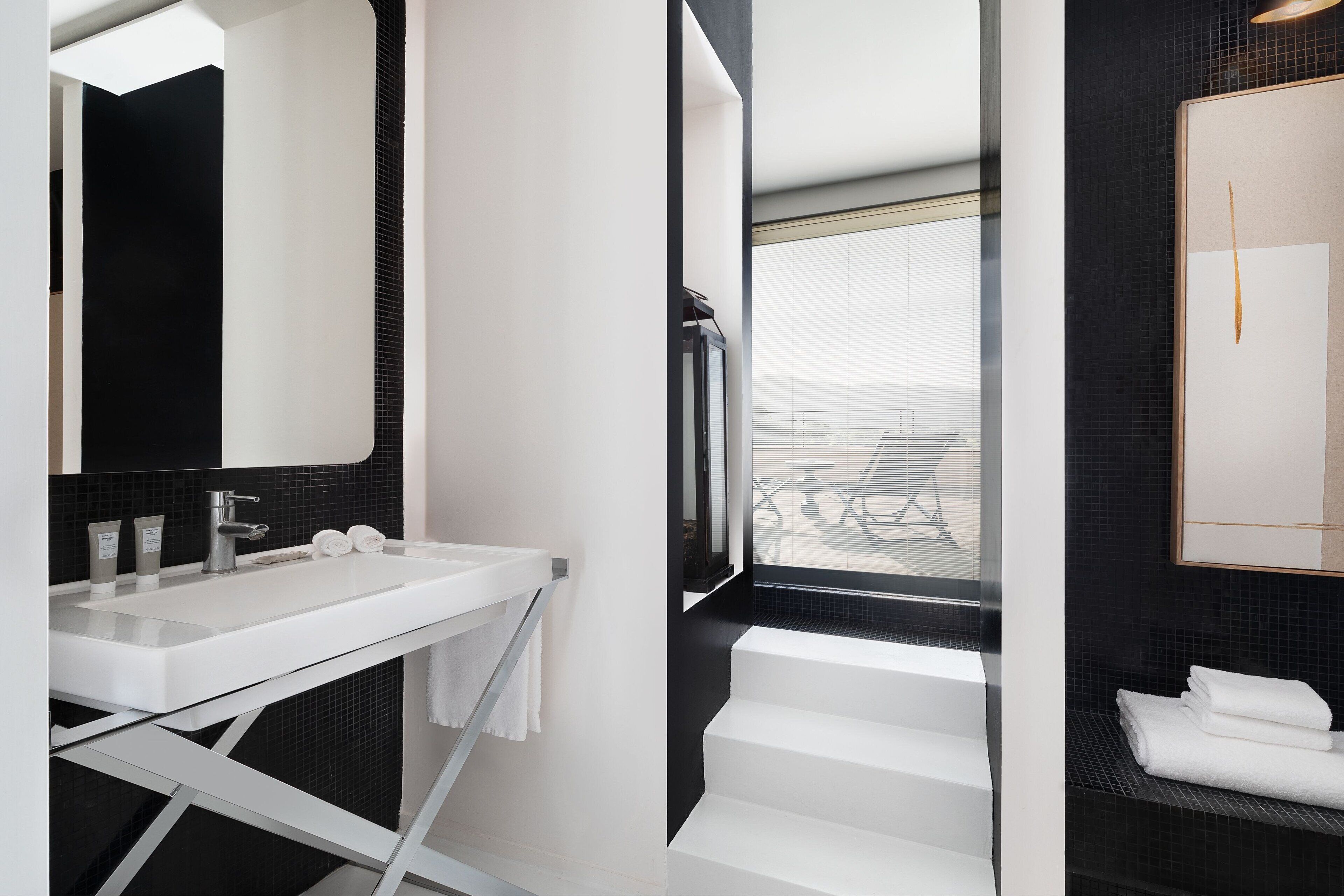 Une salle de bain moderne avec un lavabo blanc, des murs recouverts de carreaux noirs et un grand miroir.