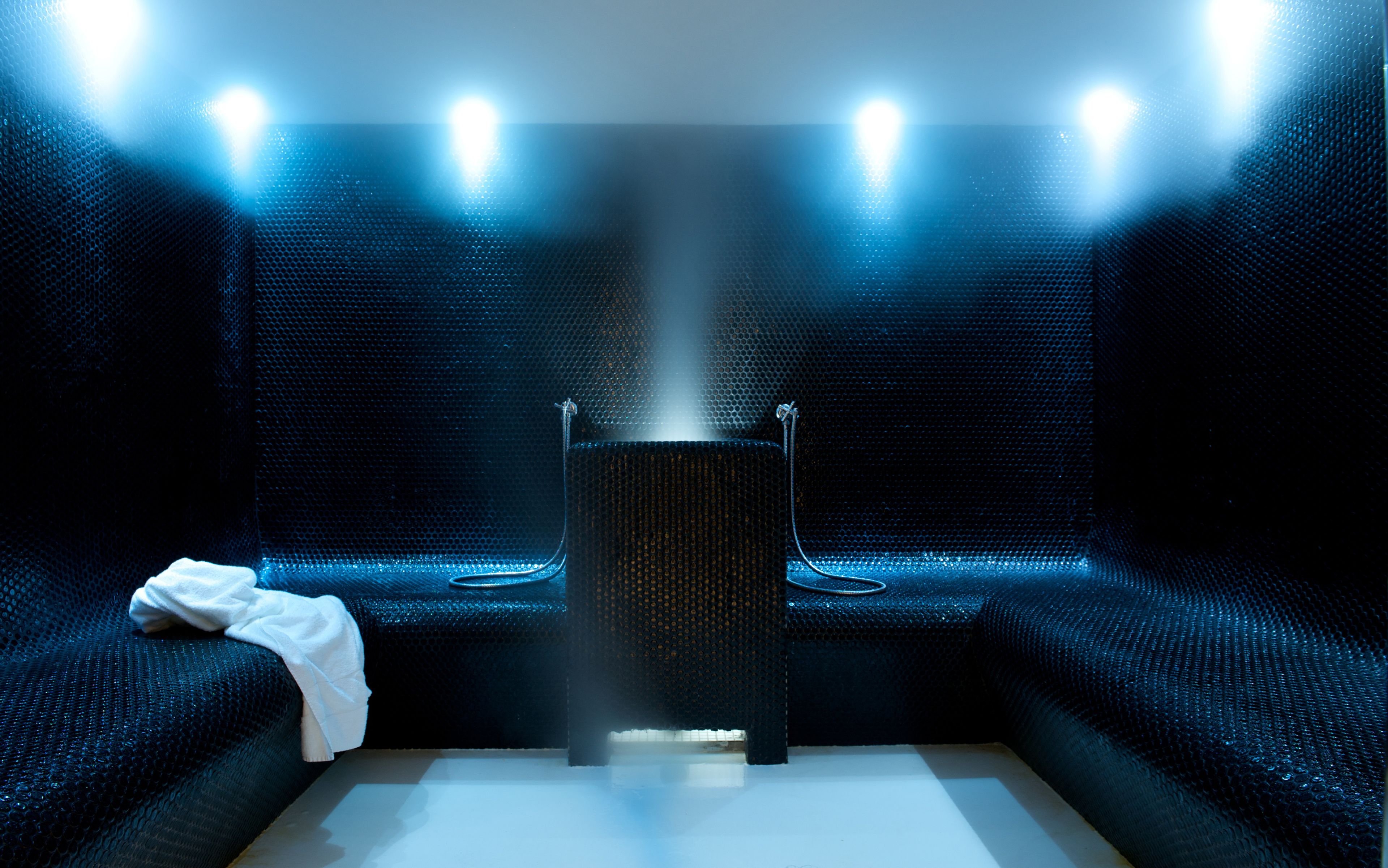 Eine Sauna mit zentralem Dampfgenerator, Bänken und einem Handtuch auf dem Boden.