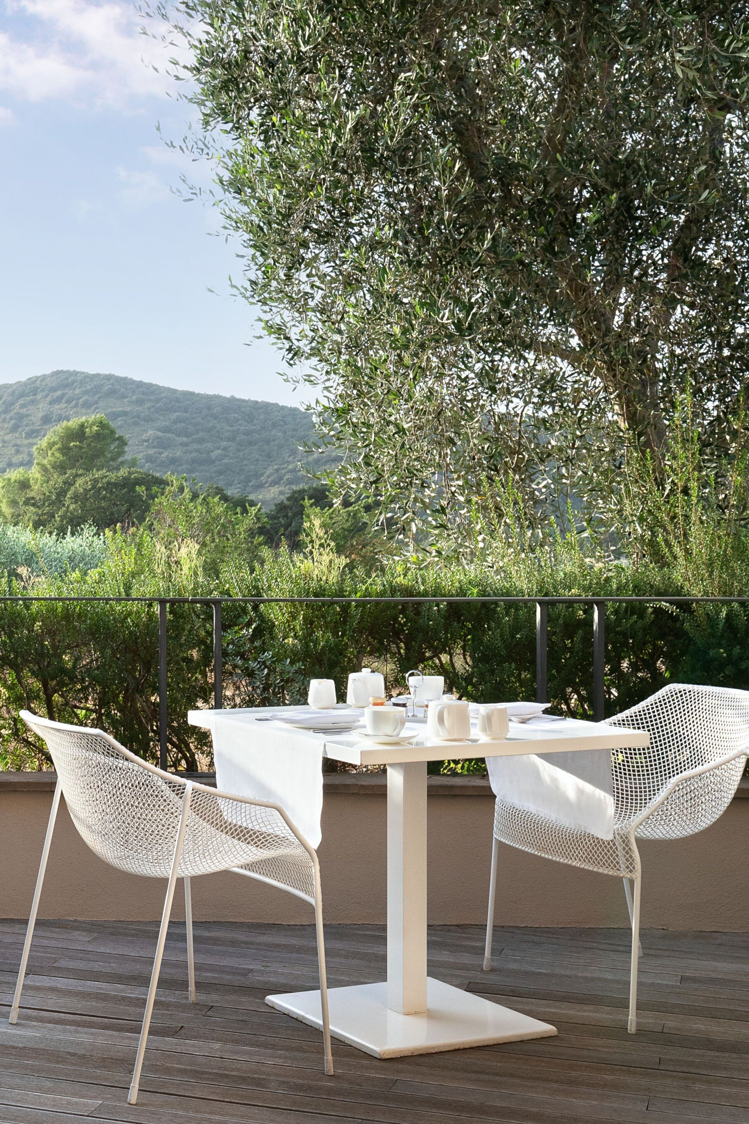 Un espace de restauration en plein air avec une table et des chaises, entouré de verdure et avec des collines en arrière-plan.