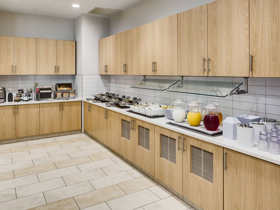 A modern kitchen with wooden cabinets, a stainless steel range hood, and a breakfast bar with various food items and drinks.