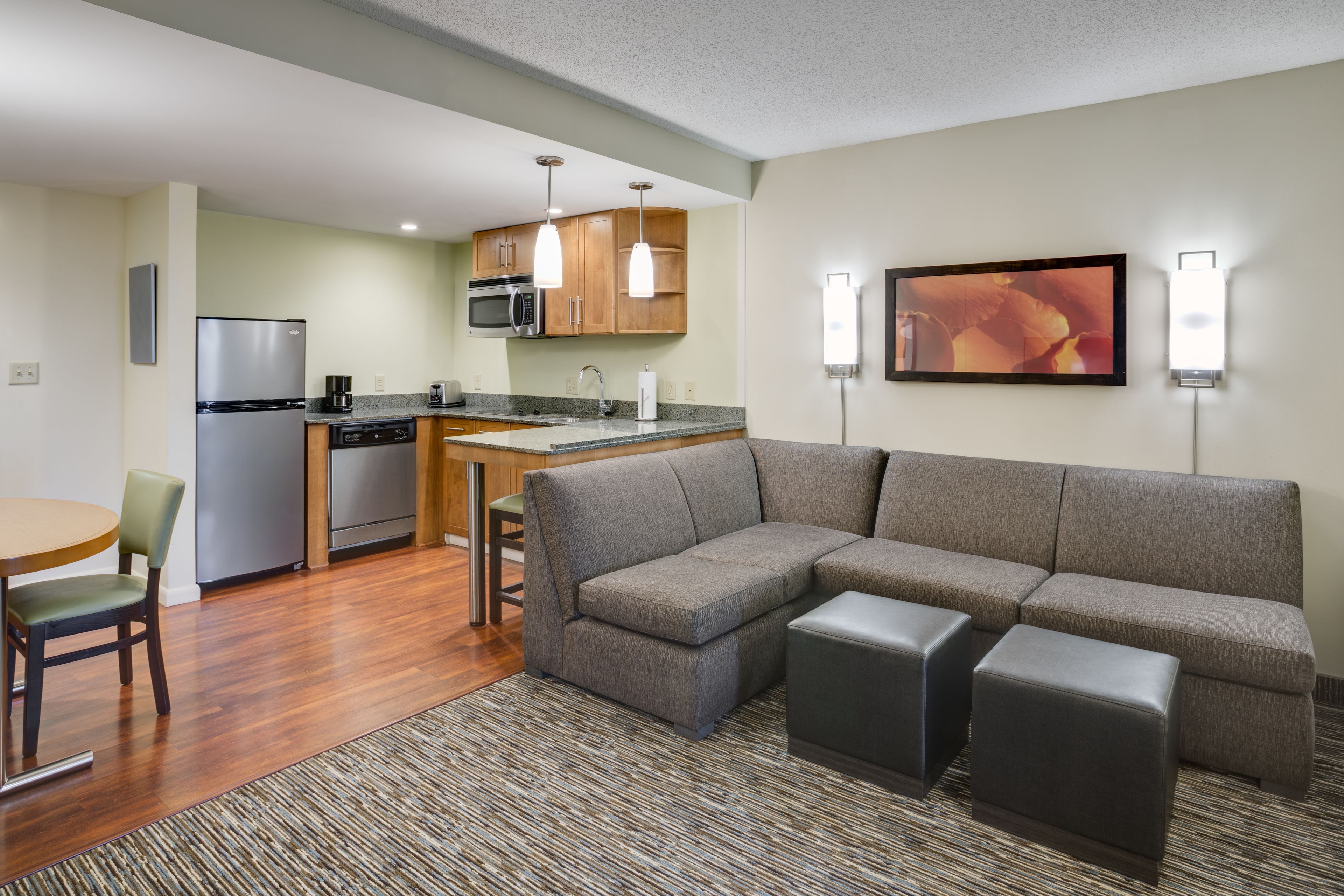 A modern kitchen with a refrigerator, microwave, and dishwasher, a gray sofa with ottomans, and a dining area with a table and chairs.