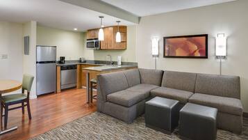 A modern kitchen with a refrigerator, microwave, and dishwasher, a gray sofa with ottomans, and a dining area with a table and chairs.