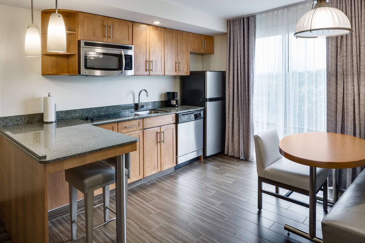 Una cocina moderna con armarios de madera, electrodomésticos de acero inoxidable y encimeras de granito, además de un comedor con una mesa redonda y sillas.