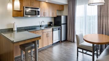 Een moderne keuken met houten kasten, roestvrijstalen apparatuur, granieten aanrechtbladen en een eethoek met een ronde tafel en stoelen.