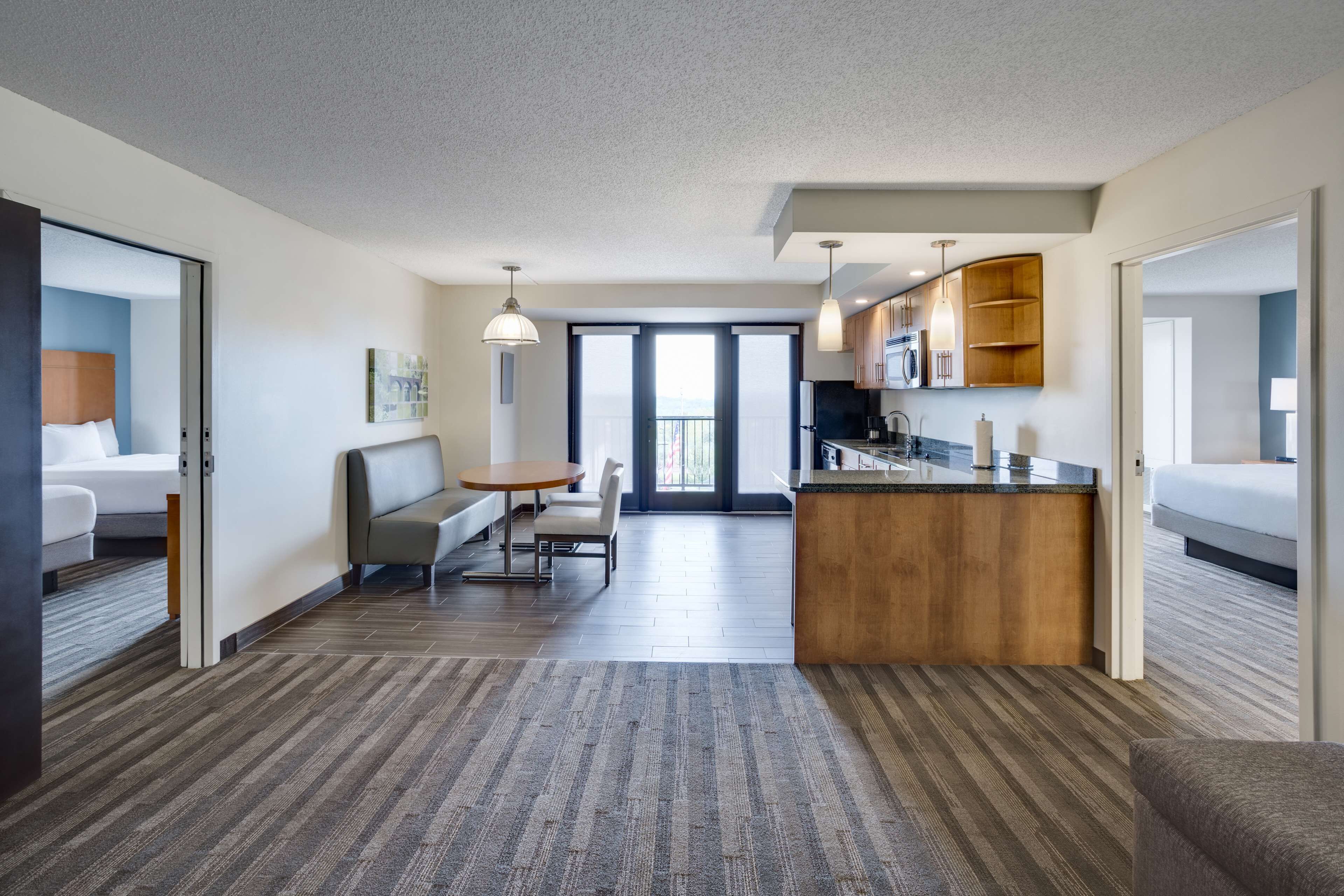 Une chambre d’hôtel moderne dotée d’une kitchenette, d’un coin repas et d’une grande porte-fenêtre coulissante donnant sur un balcon.