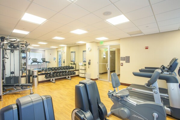 Un gimnasio con máquinas de cardio, equipo de levantamiento de pesas y mancuernas.