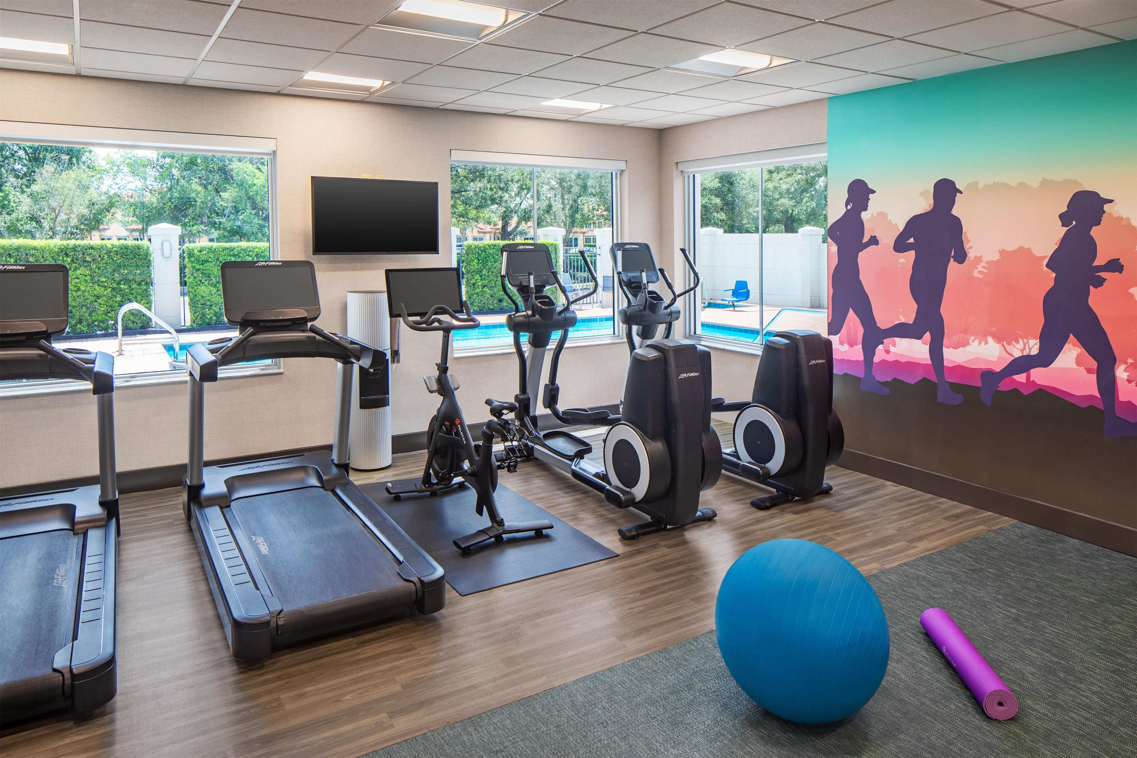 Un gimnasio con equipamiento de ejercicio, piscina y un mural de corredores.