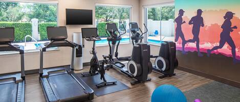 Un gimnasio con equipamiento de ejercicio, piscina y un mural de corredores.