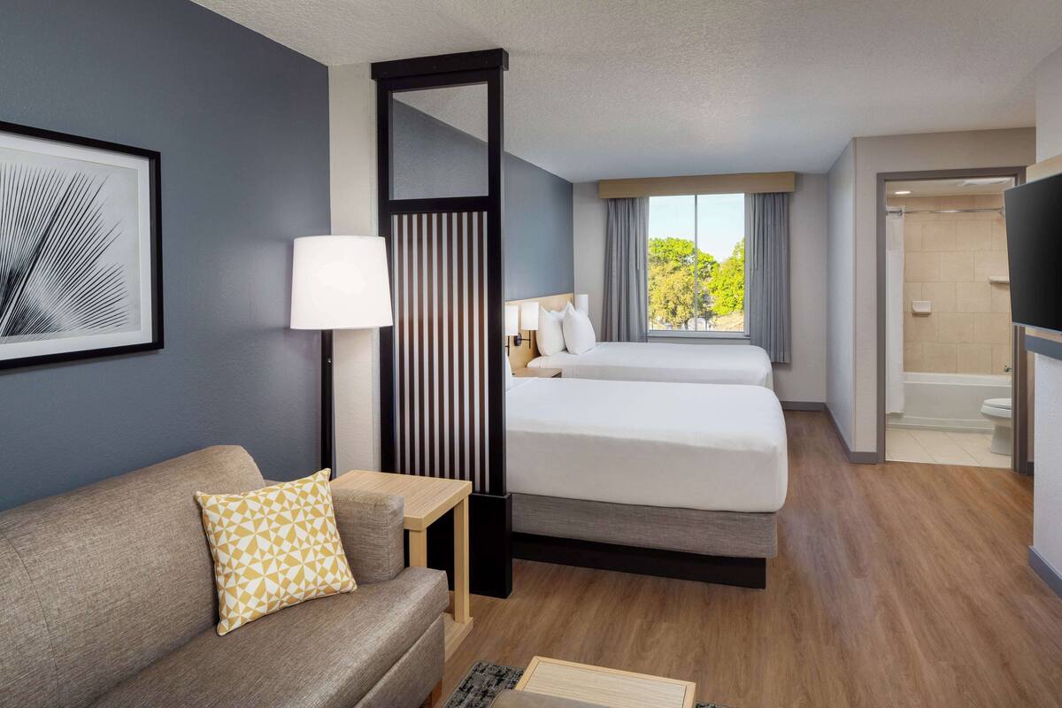 A hotel room with a sofa, two beds, a TV, a window with a view, and a bathroom.