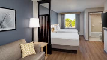Habitación de hotel con sofá, dos camas, una mesita, lámpara, espejo y vistas al exterior.