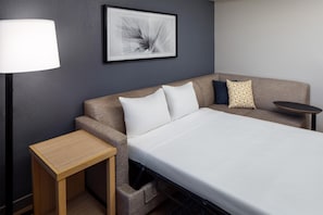 Una habitación de hotel con una cama, una mesita de noche, una lámpara, un sofá y un cuadro en la pared.