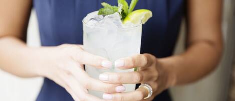 A person holding a tall glass with a lime wedge and mint leaves.