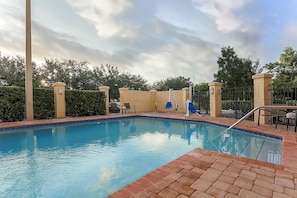Piscina con borde de ladrillo, rodeada por una valla y árboles.