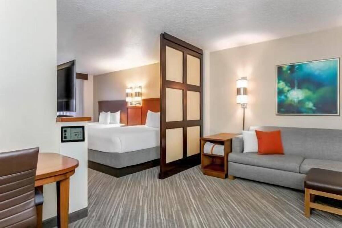 A hotel room with a bed, a sofa, a small table, a TV, and a painting on the wall.