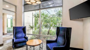 A modern interior with two blue armchairs, a small wooden table, and a large window offering a view of palm trees. - Hyatt Place Lake Mary/Orlando North (Lake Mary)