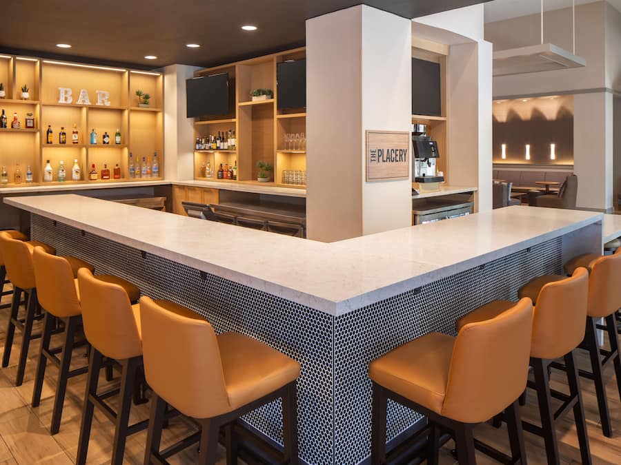 A bar area with a long counter, multiple stools, and shelves with bottles.