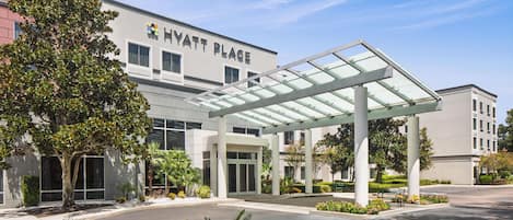 A modern hotel with a covered entrance, a landscaped driveway, and a clear sky.