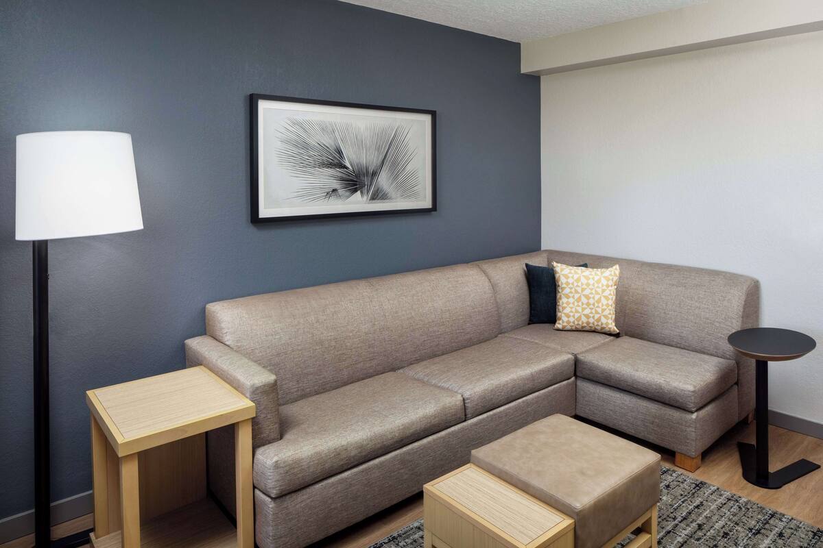 A modern living room with a sectional sofa, a small wooden side table, a round side table, and a floor lamp.