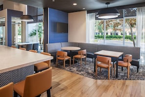 A modern restaurant interior with a bar area, seating arrangements, and large windows offering a view of the outdoors.