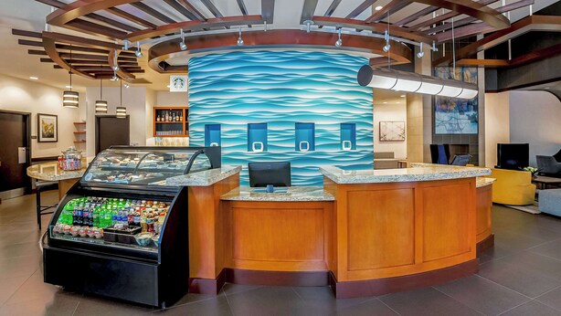 A reception area with a curved wooden counter, a glass display case with beverages, and a wall mural with a wave pattern. - Hyatt Place Lake Mary/Orlando North (Lake Mary)