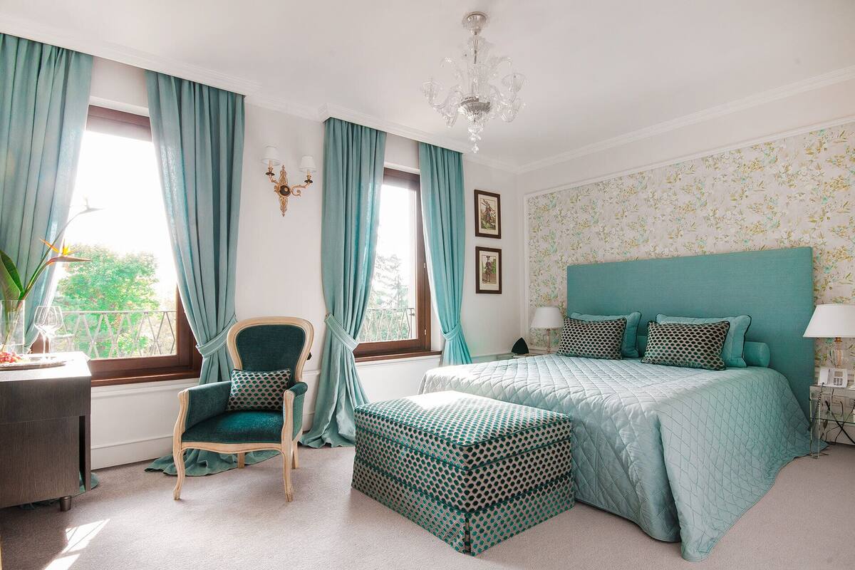 A bedroom with a bed, a chair, a desk, and a window with curtains.