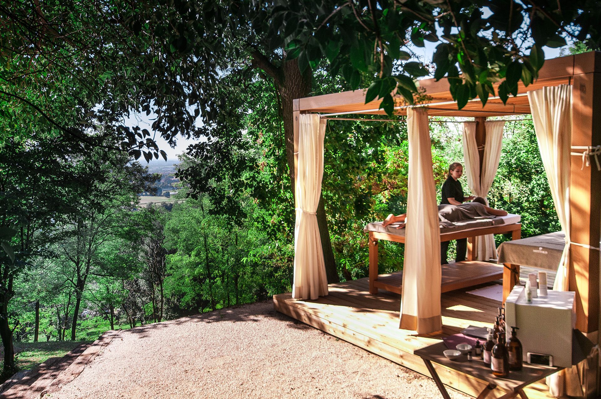 Un'area massaggi all'aperto in legno con un tetto a baldacchino, immersa nel verde e con vista panoramica.
