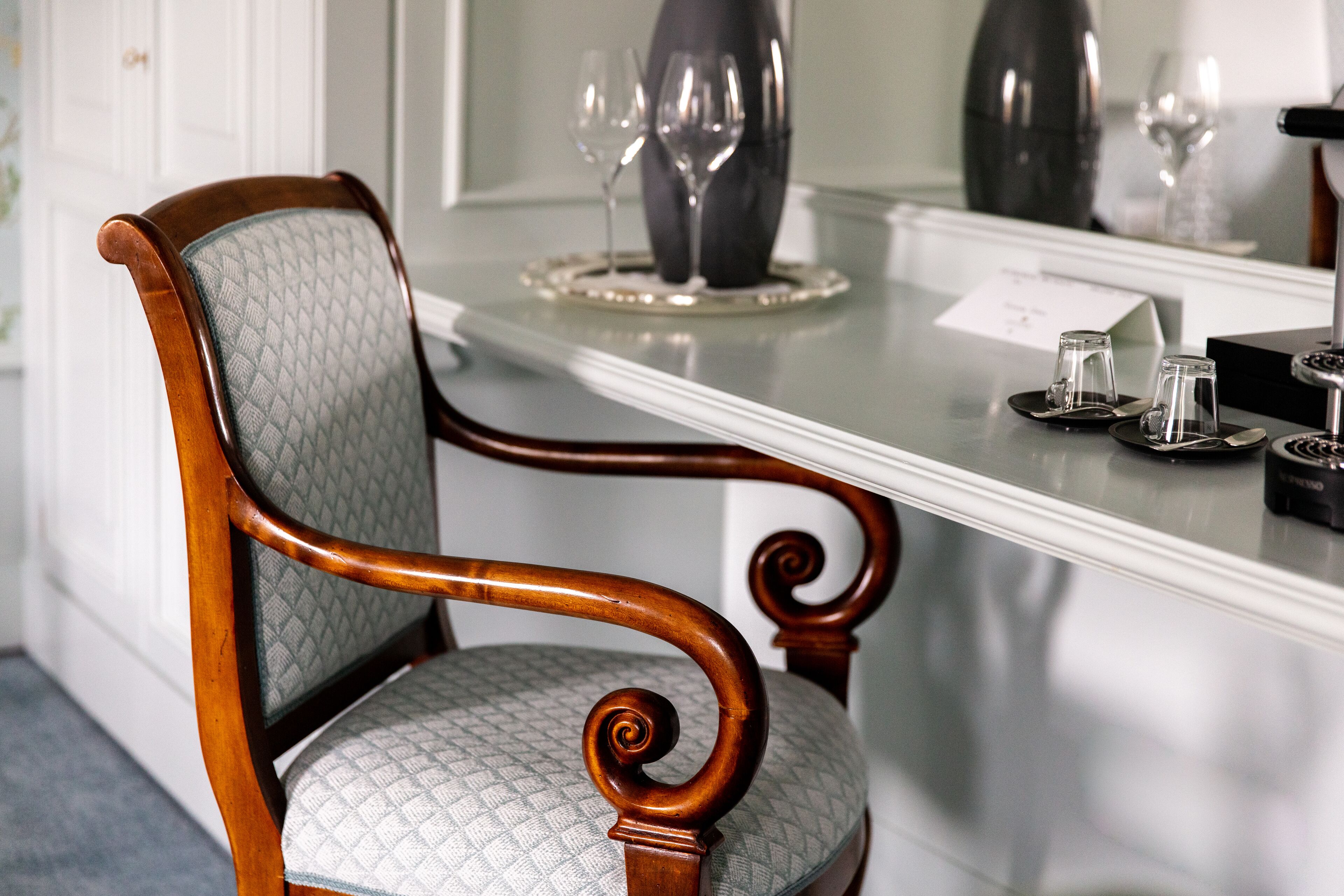 A wooden chair with a cushioned seat and backrest, positioned in front of a table with a glass top.