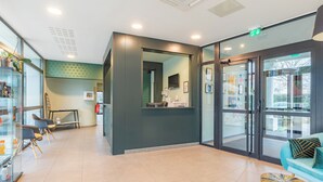 A modern reception area with a glass door entrance, a reception desk, seating area with a sofa and chairs, and a small table with a decorative item. - Appart’City Confort Toulouse Purpan (Toulouse)
