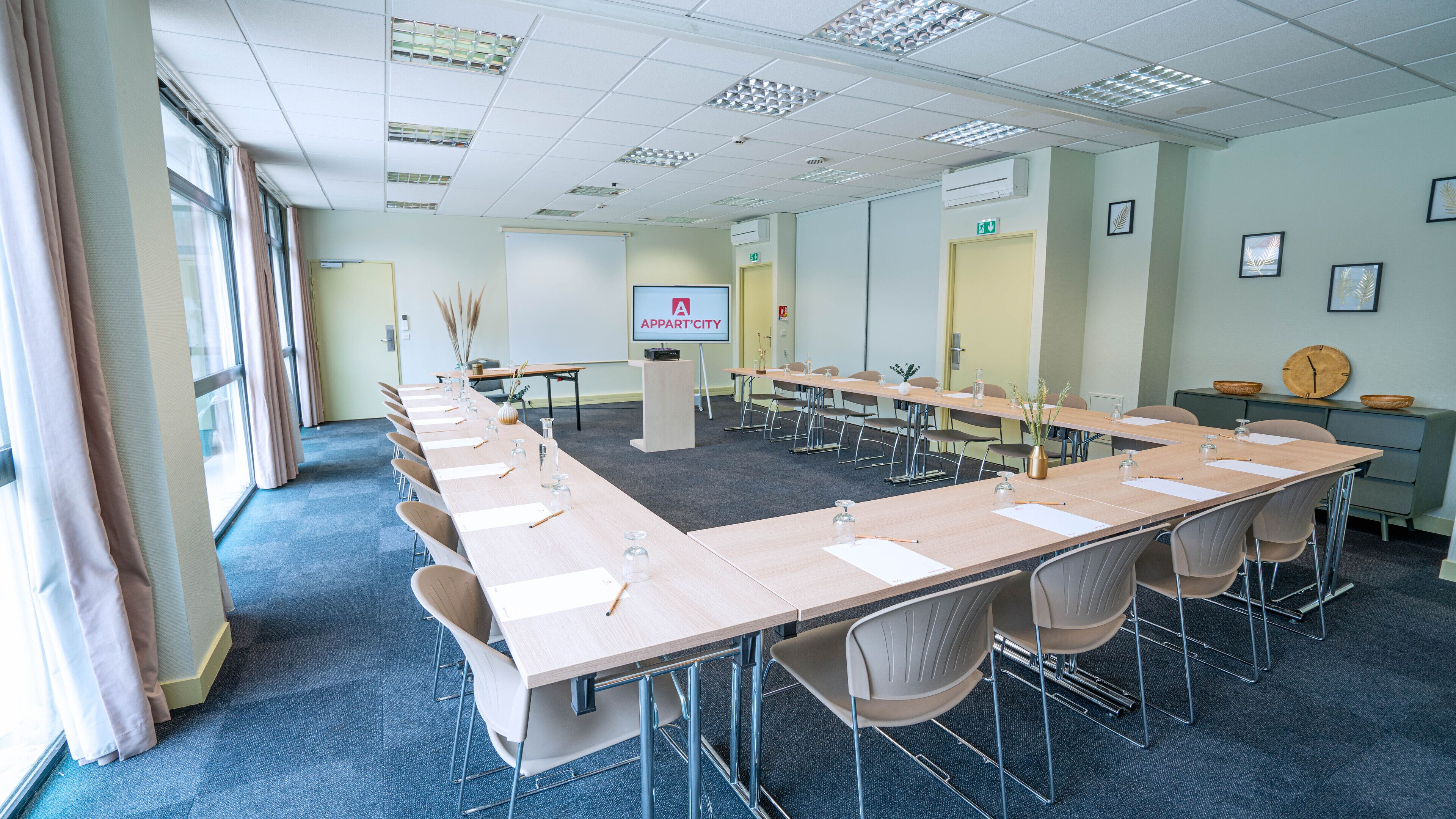 A conference room with a long table, chairs, a projector screen, and a clock on the wall.