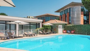 A swimming pool with lounge chairs and umbrellas, surrounded by buildings with large windows and a brick facade. - Appart’City Confort Toulouse Purpan (Toulouse)