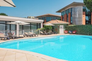 A swimming pool with lounge chairs and umbrellas, surrounded by buildings with large windows and a brick facade.