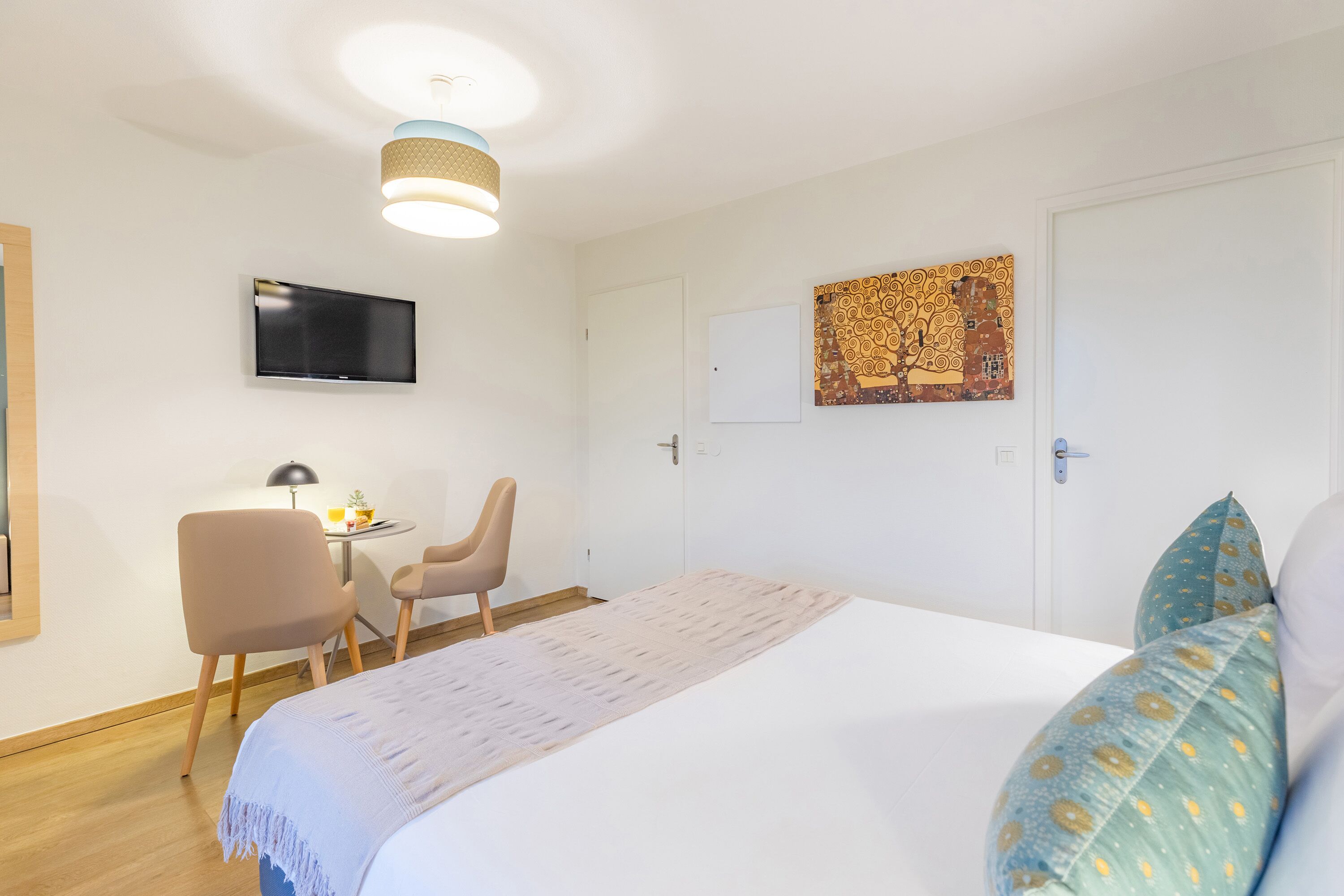 Ein Schlafzimmer mit einem Bett, einem Schreibtisch, zwei Stühlen, einem Fernseher und Bildern an der Wand.