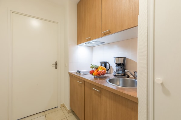 Una pequeña cocina con armarios de madera, un lavamanos de acero inoxidable y un frutero sobre la encimera.