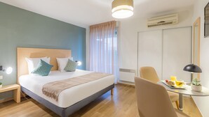 A modern hotel room with a large bed, bedside table, and a desk with a chair. - Appart’City Confort Toulouse Purpan (Toulouse)