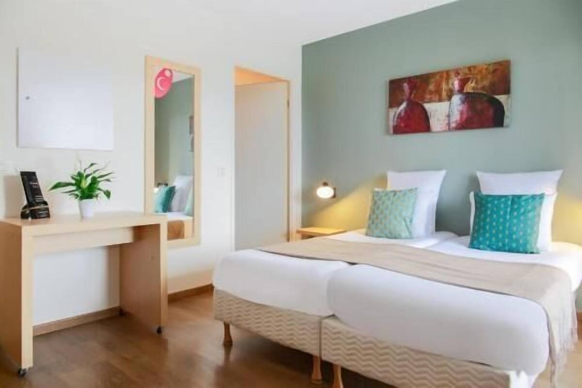 A bedroom with a bed, bedside table, lamp, and a painting on the wall.