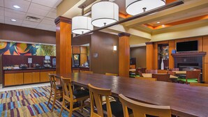 A hotel dining area with a long wooden table, multiple chairs, a patterned carpet, and a television mounted on the wall. - Fairfield Inn & Suites Cookeville (Cookeville)
