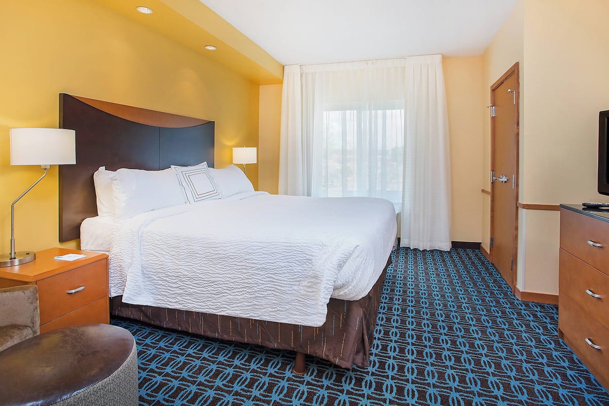 Una habitación de hotel con una cama grande, un escritorio con lámpara, una silla y un armario.
