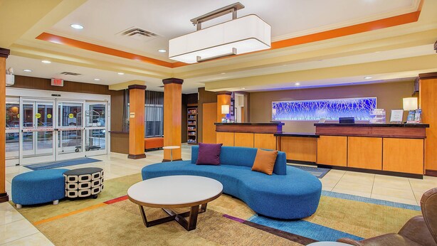A hotel lobby with a reception desk, a blue sofa, a round table, and a seating area with a brown chair. - Fairfield Inn & Suites Cookeville (Cookeville)